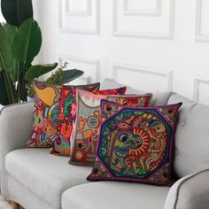 three colorful pillows sitting on top of a gray couch next to a potted plant