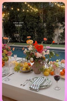 the table is set with flowers and fruit for an outdoor dinner by the swimming pool