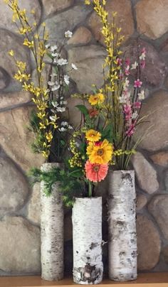 three vases filled with flowers sitting on top of a wooden table next to a stone wall