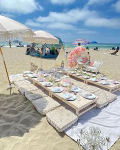 a table set up on the beach with plates and drinks under an umbrella for people to enjoy