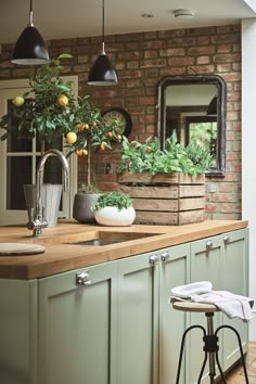 a kitchen with green cabinets and wooden counter tops next to a brick wall that has potted plants on it