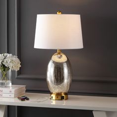 a lamp on a table next to a book and vase with white flowers in it