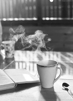 a coffee cup with steam rising out of it sitting on a table next to an open book