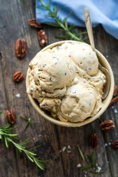 two scoops of ice cream in a bowl with pecans and rosemary on the side