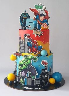 a multi - tiered cake decorated with superheros and balloons