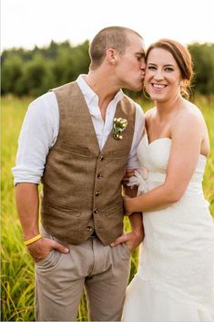 a bride and groom kissing in the middle of a field with tall grass behind them