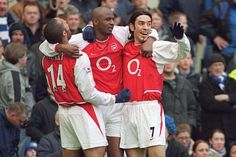 three men in red and white soccer uniforms are hugging each other on the sidelines