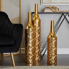 two gold vases sitting next to each other in front of a black chair and table