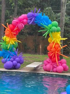 an outdoor pool with balloons and streamers in the shape of a rainbow colored arch