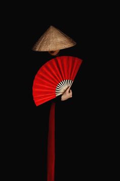 a woman with a red fan and a straw hat on her head is standing in the dark