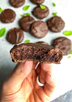 a person holding up a chocolate cookie in front of some mint sprig leaves