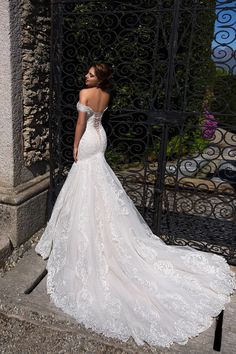 a woman in a white wedding dress standing on the steps near an iron gate with her back turned to the camera