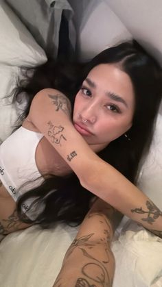 a woman laying in bed with tattoos on her arm