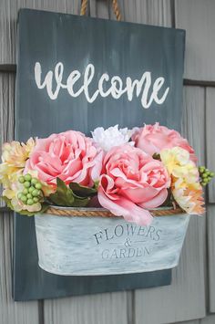 a welcome sign hanging on the side of a building with pink and white flowers in it