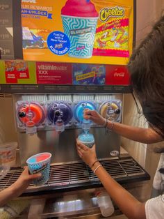 two girls are playing with cups in front of a vending machine that sells frozen drinks