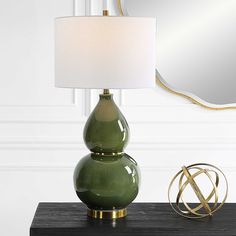 a green lamp sitting on top of a wooden table next to a mirror and a gold sculpture