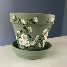 a green flower pot with white flowers painted on it