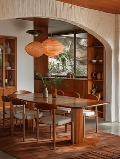 a dining room table surrounded by chairs and wooden shelves with plants in vases on them