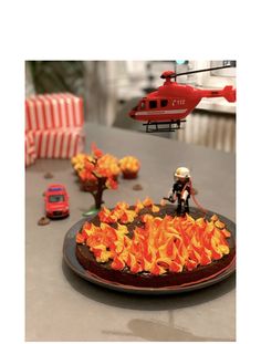 a toy helicopter is flying over a pizza on a table with fire and flames around it