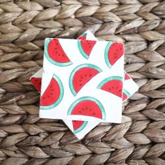 two pieces of paper with watermelon designs on them sitting on a woven basket