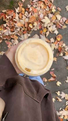 a person holding a cup of coffee in front of some leaves on the ground with their hands