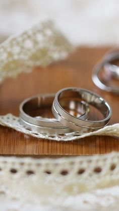 two silver wedding rings sitting on top of a wooden table next to a lace doily