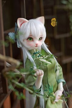 a doll with white hair wearing a green dress and holding a branch in her hand