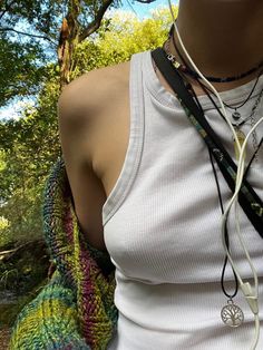 a woman wearing a white tank top holding a cell phone in her hand while standing next to a tree