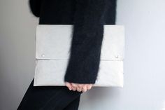 a woman is holding a white and black clutch on her hand while standing against a wall