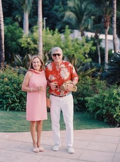 an older man and woman standing next to each other in front of some palm trees