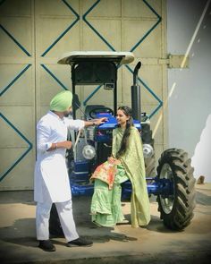 a man standing next to a woman in front of a tractor with a green turban