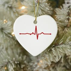 a white heart ornament with a red heartbeat on it hanging from a christmas tree