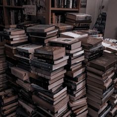 a large stack of books sitting on top of a wooden table next to a window