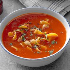 a bowl of tomato soup with pasta and parsley on the side, next to a bottle of ketchup