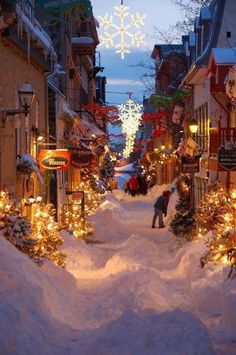 a street is covered in snow and lit up with christmas lights as people walk down it