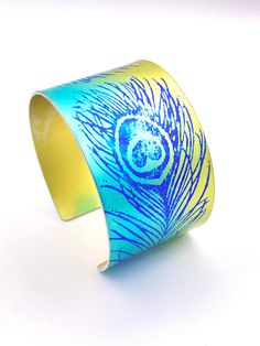 a blue and yellow bracelet with a peacock print on it's side, sitting on a white surface