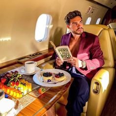 a man sitting in an airplane reading a book with fruit on the table next to him