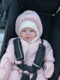 a small child in a pink coat sitting in a stroller