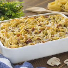 a casserole dish filled with pasta and mushrooms on a wooden table next to flowers