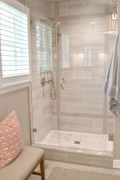 a walk in shower sitting next to a white bench and window with blinds on it