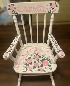 a white rocking chair with pink roses painted on the back and name charlotte written on it