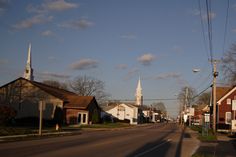 an empty street with houses and church spires in the background