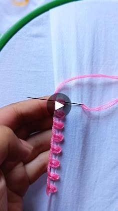 someone is stitching pink thread on a white piece of fabric with a green needle