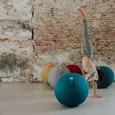 a person doing a handstand on top of balls in front of a brick wall