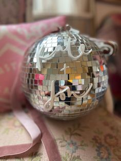 a disco ball sitting on top of a table next to a pink ribbon and pillow