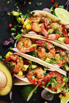 three shrimp tacos with avocado and cilantro on a black plate