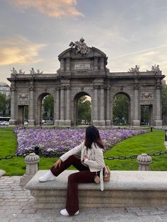 a woman sitting on a stone bench in front of a building with arches and flowers