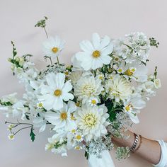 a person holding a bouquet of white flowers in their left hand and wearing bracelets