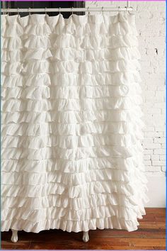 a white shower curtain with ruffles hanging from it's side in front of a brick wall