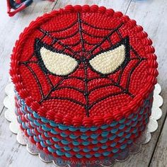 a spiderman cake is decorated with red, white and blue icing on a wooden table